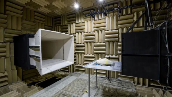 Anechoic chamber interior with foam panels, a large speaker, and a metal table with an object.