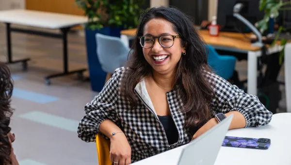 A student smiling while sat at a desk on a university campus.