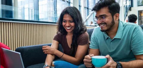 Two students huddle around a laptop together checking information on the screen.