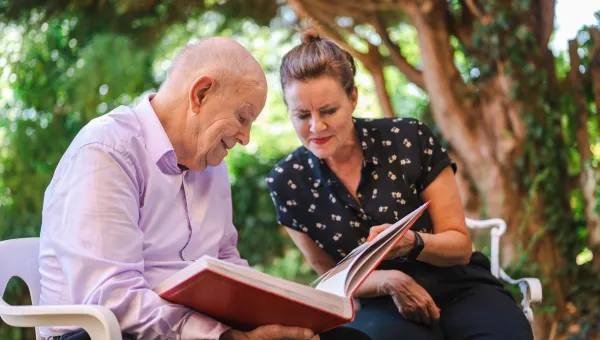 A woman and an elderly man sat in a park looking at a book together