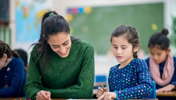 Adult sat with a child at a school desk with a drawing