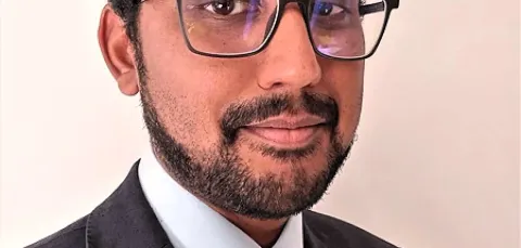 Dr Varatharaj looks out at the camera wearing a black suit and tie