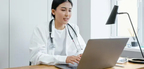 A doctor sits at a laptop doing research