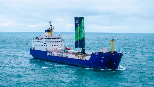 A large cargo vessel sailing on the ocean. It has a 20 metre-high wing sail. 