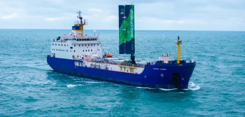 A large cargo vessel sailing on the ocean. It has a 20 metre-high wing sail.