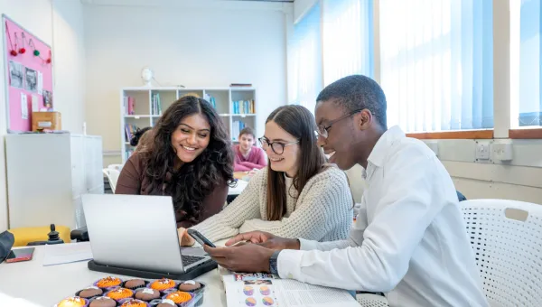 Students smiling looking at a laptop in a classroom.