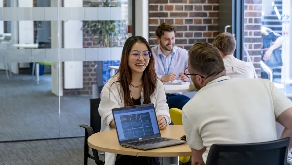 A student discussing fees with a university advisor. Another student and advisor talking are in the background.