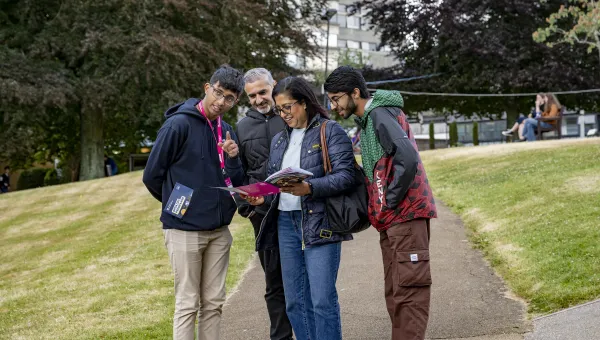 An applicant and their parents at an open day, speaking with a student advisor. They are looking at a prospectus and pointing behind the camera.