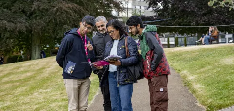 An applicant and their parents at an open day, speaking with a student advisor. They are looking at a prospectus and pointing behind the camera.
