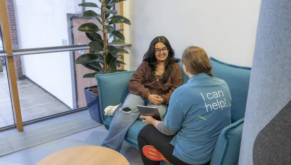 A student discussing support options with a Student Hub advisor while sat on a sofa.