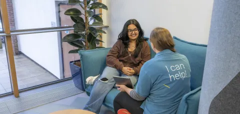 A student discussing support options with a Student Hub advisor while sat on a sofa.