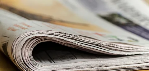 A rolled-up newspaper on a wooden surface, with visible pages and text.