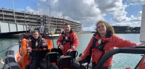 Three instructors standing on a powerboat moored at the quay side. They are all and looking directly at the camera. You can see the multistorey cruise parking building in the background.