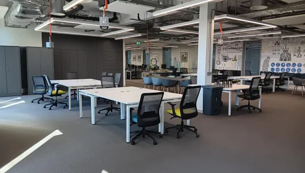 Modern open office space with white desks, black chairs, grey cabinets, and a collaborative area with murals.
