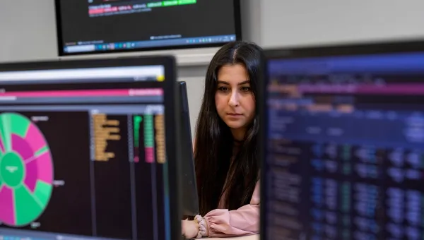 A student is surrounded by Bloomberg terminals, showing data in various colourful representations. 