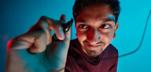 A student using a black marker pen to draw a line on a glass screen. The student is wearing a dark red t-shirt and is positioned in front of a blue background.