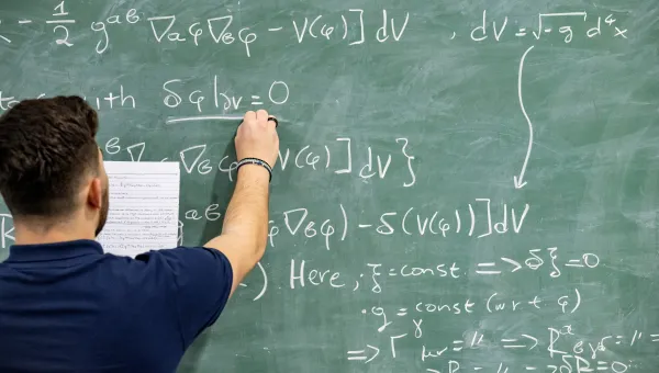 A student writing a complex mathematical equation on a blackboard
