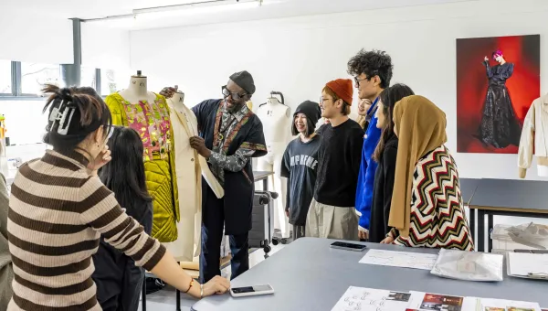 Fashion design tutor presenting a garment to a group of students in a studio.