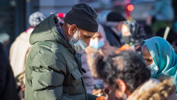 People wearing masks gather outdoors, some handing out fruit during a community food distribution.