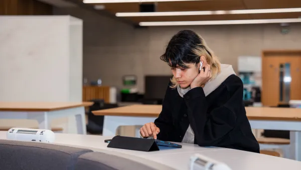 A student using a tablet and wireless earphones.