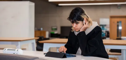 A student using a tablet and wireless earphones.