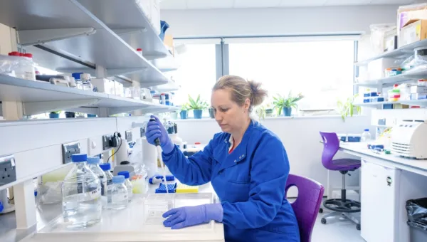 Dr Jemma Longley is wearing a blue lab coat working with a pipette in a bright laboratory.