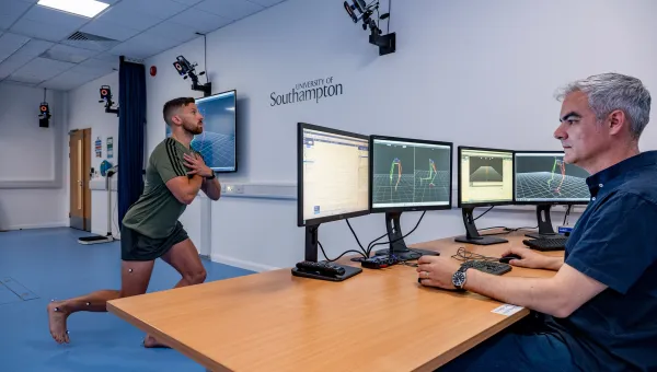 A man performs a lunging squat with motion capture markers, while another man monitors data on screens in a lab.