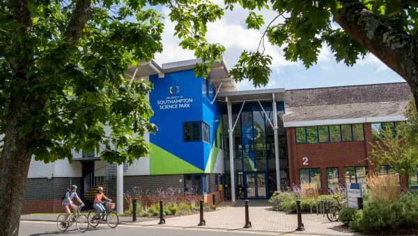 An exterior view of the main building at the Science Park. It is a sunny day and there are 2 cyclists on the road in front of the building.