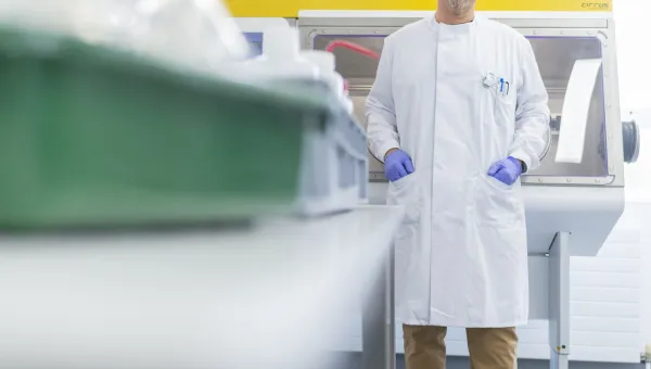 Person in a lab coat standing in a laboratory near a fume hood.