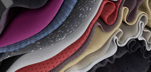 A close-up view of layered, folded fabrics in different colours and textures, shown in a wavy, rippled arrangement.