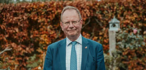 Portrait of Professor Stephen Holgate in a blue suit standing outdoors in front of autumn foliage.