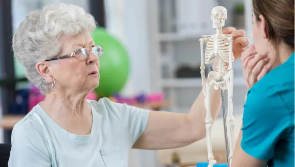 A woman looking at a table top hanging human sketeton.