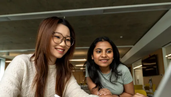 Two international students research courses on a laptop