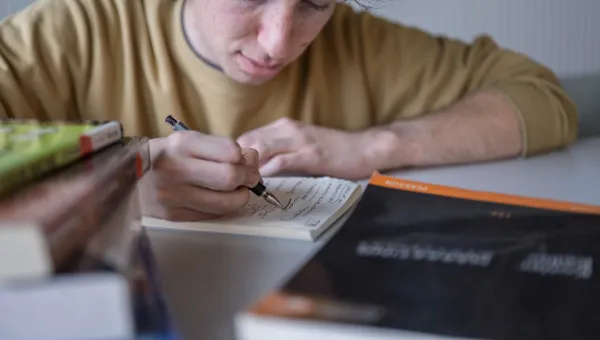 A student leans over a notebook where he writes down questions to ask later