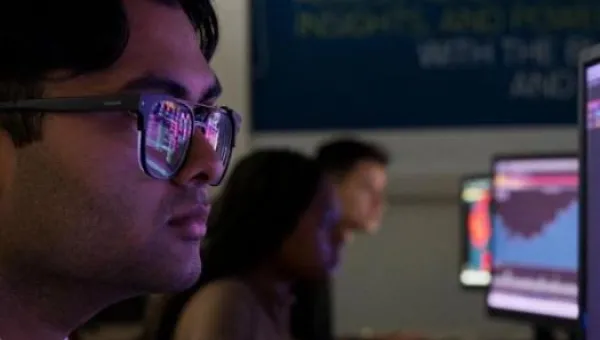 A student in the foreground looks intently at his PC screen, business analytics reflected in his glasses