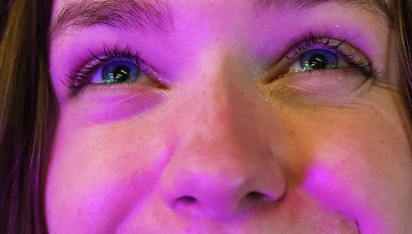 The camera leans close to the face of a student bathed in a warm purple light. She looks up, smiling expectantly