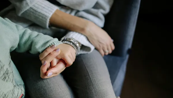 Two pairs of hands intertwined, the child is wearing a mint-green sweater with bracelets on the wrist, and the other in a light grey sweater, in a cosy setting.