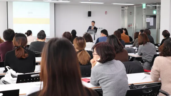 A lecturer stands in front of a classroom of students