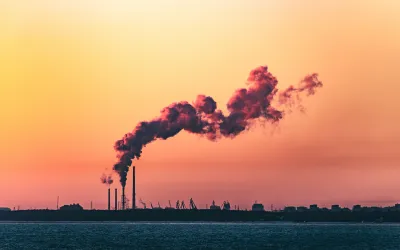 A shot of an industrial shoreline silhouetted at sunset, with smoke from a refinery curling into the sky.