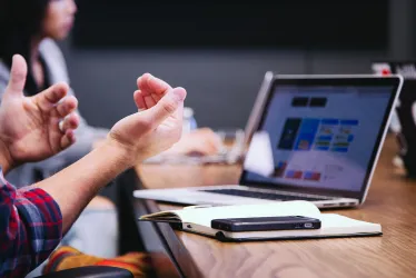 Laptop on a table with notepad and phone, user's hands in foreground 