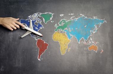 Image of a world map and a person holding a model aeroplane above it.
