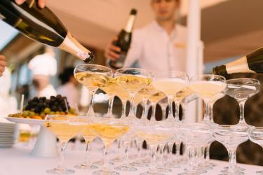 Image of pyramid of champagne glasses being poured into by a waiter. 