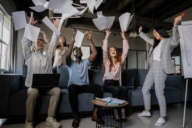 A diverse group of business people throw sheets of paper in the air