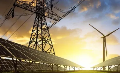 A low-angle view of solar panels, a wind turbine and a pylon, with the sun rising in the background