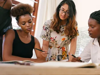 Diverse group of women collaborating round a table, using pens and paper