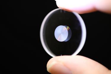 A small optical lens held between a finger and thumb