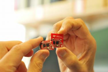 Hand holding a red internet of things circuit board created by the Centre for IoT and Pervasive Systems. 