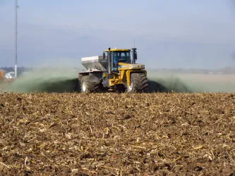 A tractor scattering crushed rock as it drives across a field.