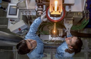 View from above of two researchers feeding glass into a fibre drawing furnace.