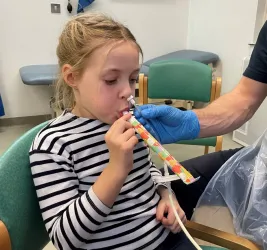 Young girl with a tube up her left nostril, blowing a party blower